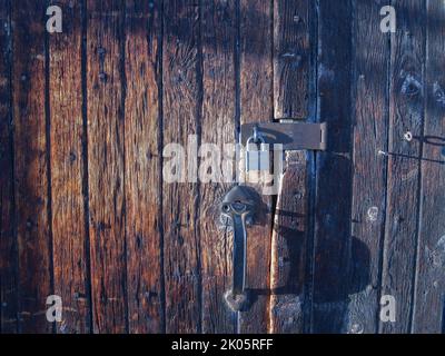 Old wooden door made of vertical planks worn and faded with padlock and handle. Stock Photo