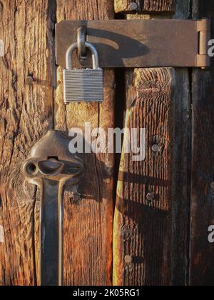 Old wooden door made of vertical planks worn and faded with padlock and handle. Stock Photo