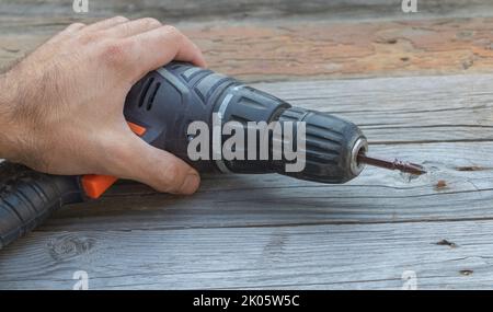 Humand handusing screwdriver on wooden table - From above of crop anonymous person using electric screwdriver while working in workshop Stock Photo