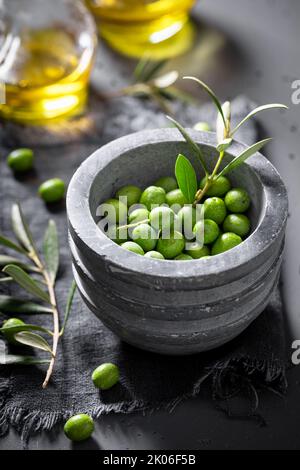 Green and small raw olives with mortar and a twig. Freshly picked green olives. Stock Photo
