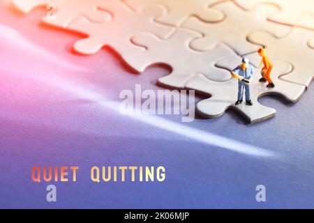 Single tiny worker miniature figure on edge of linked jigsaw puzzle. Blue purple gradient paper background, long shadow, flare. Concept background. Stock Photo