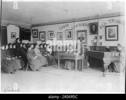 Debating class, Carlisle Indian School, Carlisle, Pennsylvania, 1901. A young woman standing before a group of seated students. A partially visible chalkboard says &quot;Debate. Resolved: That the U.S. Senate ...&quot; An older woman is seated at a piano on the right. The motto &quot;Labor conquers all things&quot; and framed portraits featuring women are on the wall. (Boarding school for Native American students, founded in 1879 under US governmental authority). Stock Photo
