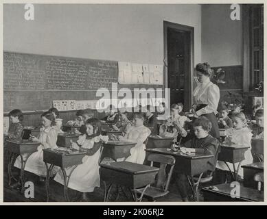 Pattern making, 1900. A group of school children cutting paper into leaf shapes, as their teacher looks on. In pamphlet: The new education illustrated. Stock Photo