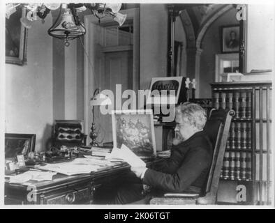 John Willock Noble, 1831-1912, between c1890 and c1910. Three-quarter length portrait, seated at desk, left profile. [Politician, lawyer, brigadier general in the Civil War. Note framed photograph of Native Americans on desk. 'Under his watch as Secretary of the Interior, the Cherokee Commission negotiated eleven agreements that removed nineteen indigenous tribes to small allotments in the Oklahoma Territory, while opening the land to homesteaders']. Stock Photo