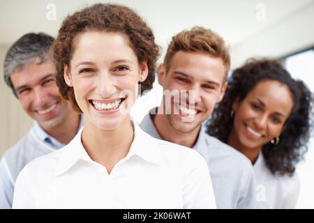 Hard working and happy. Closeup portrait of a positive-looking young professional with her coworkers standing behind her. Stock Photo