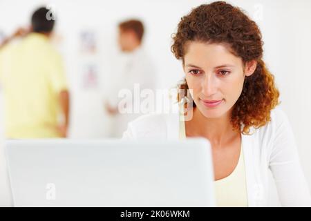Cute business woman using laptop. Closeup of cute business woman using laptop with colleagues in background. Stock Photo