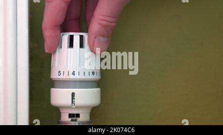Hand turning down radiator heating to save money Stock Photo