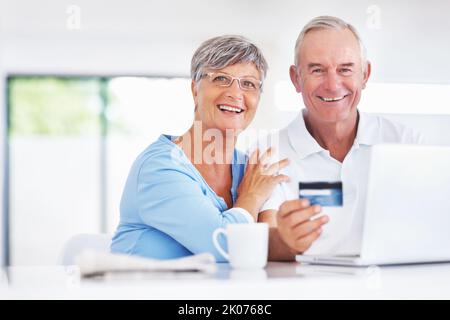 Happy mature couple shopping online. Portrait happy mature couple shopping online using credit card and laptop. Stock Photo