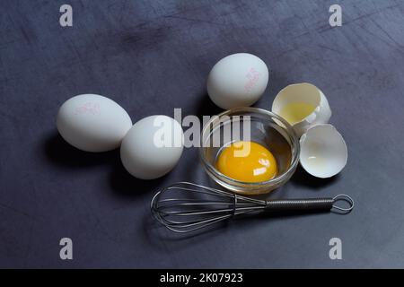 Egg yolks in small bowls and egg whites in egg shells, whisk Stock Photo