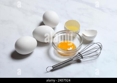 Egg yolks in small bowls and egg whites in egg shells, whisk Stock Photo