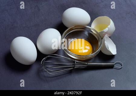 Egg yolks in small bowls and egg whites in egg shells, whisk Stock Photo