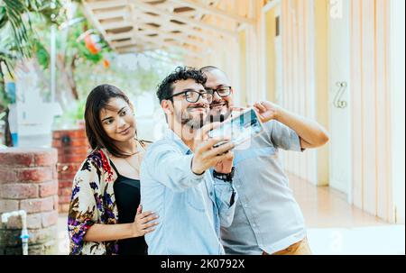 Three friends taking a selfie outside, Three smiling friends taking a selfie on the street. Front view of three cheerful friends taking a selfie on Stock Photo