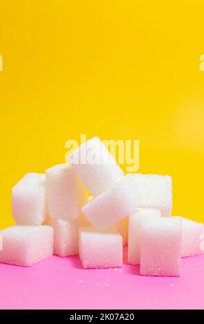 Sugar cubes, stack of sugar cubes isolated on yellow and pink background. Unhealthy sweet food idea concept. Vertical photo. No people, nobody. Stock Photo