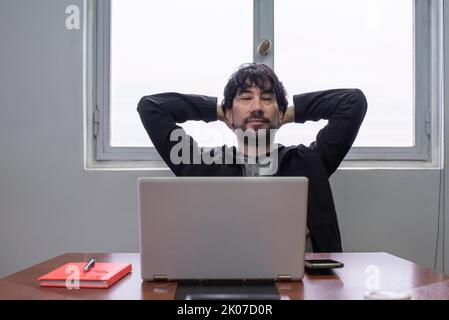Relaxed businessman at the work desk, positive calm, holding hands behind his head and with eyes closed Stock Photo