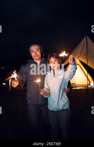 Happy Chinese couple holding sparklers and camping outdoors Stock Photo