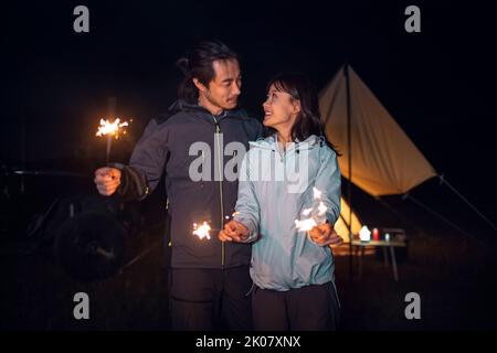 Happy Chinese couple holding sparklers and camping outdoors Stock Photo