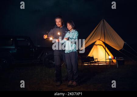 Happy Chinese couple holding sparklers and camping outdoors Stock Photo