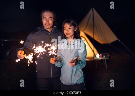Happy Chinese couple holding sparklers and camping outdoors Stock Photo