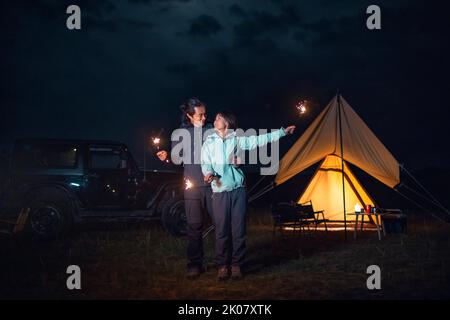 Happy Chinese couple holding sparklers and camping outdoors Stock Photo