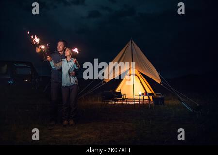 Happy Chinese couple holding sparklers and camping outdoors Stock Photo