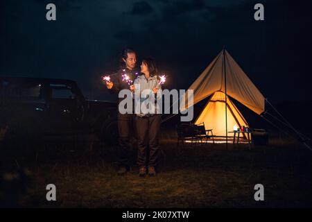 Happy Chinese couple holding sparklers and camping outdoors Stock Photo
