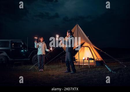 Happy Chinese couple holding sparklers and camping outdoors Stock Photo