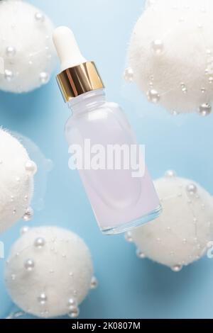 Christmas minimalistic composition with brown glass serum bottle on blue background with flying golden christmas balls. Health and beauty concept. Stock Photo