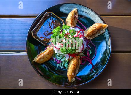 Deep fried Asian dumplings, Japanese gyoza or Chinese jiaozi, served with salad, sauce and parsley garnish on a dark plate, copy space, high angle vie Stock Photo