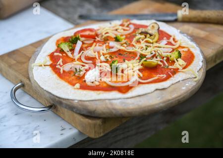 Fresh whole grain pizza with tomato sauce, broccoli, onions and cheese, prepared for baking on a wooden kitchen board, healthy vegetarian food, select Stock Photo