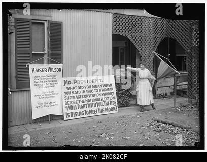 Woman suffrage banners, between 1916 and 1918. First World War: woman pointing at banners reading: 'Kaiser [Woodrow] Wilson, have you forgotten your sympathy with the poor Germans because they were not self-governed? 20,000,000 American women are not self-governed. Take the beam out of your eye'. 'Mr President, what did you mean when you said in 1916 to a woman suffrage convention, shortly before the national election: &quot;I will fight with you. The tide is rising to meet the Moon&quot;?'. Note pile of banners and poles for demonstrations. Women in the United States gained the legal right to Stock Photo