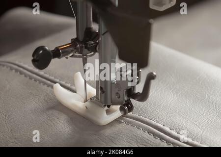 Modern sewing machine with special presser foot makes a seam on grey leather. sewing process close up Stock Photo