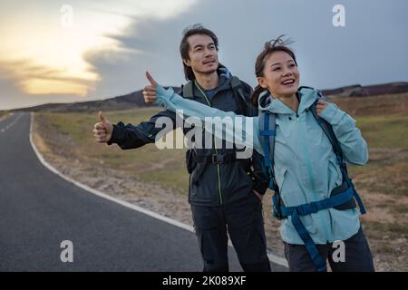 Happy Chinese couple hitchhiking on the road Stock Photo