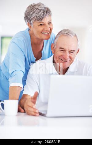 Smiling mature couple using laptop at home. Smiling mature man using laptop at home with woman looking at screen. Stock Photo