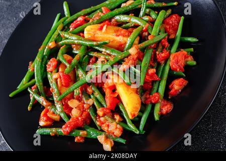 fasolakia lathera, green beans, onion and potatoes stewed in tomato, herbs and olive oil on black plate, greek cuisine, close-up Stock Photo