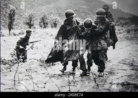 Capt. Emil Kapaun (right), former chaplain with Headquarters Company, 8th Cavalry Regiment, 1st Cavalry Division, helps another soldier carry an exhausted Soldier off the battlefield early in the Korean War. Stock Photo