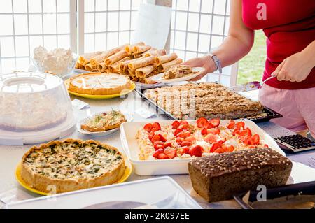 Close up view of person selling homemade pastry and cakes at home cafe day event. Person hands holding and giving cake to customer. Various cakes. Stock Photo