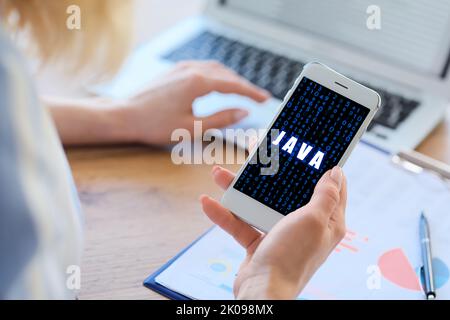 Young female programmer with mobile phone and laptop in office Stock Photo