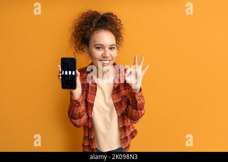 Young woman holding mobile phone with word JAVA on screen against orange background Stock Photo