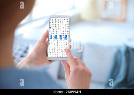Young woman holding mobile phone with word JAVA on screen in room Stock Photo