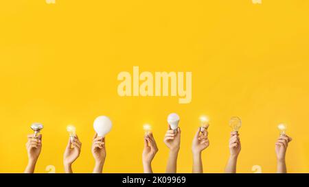 Many hands with different light bulbs on yellow background Stock Photo