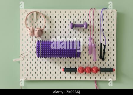 Pegboard with sports equipment and headphones on green wall Stock Photo