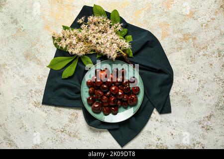 Plate with chestnuts and flowers on light background Stock Photo