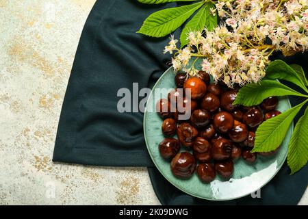 Plate with chestnuts and flowers on light background Stock Photo