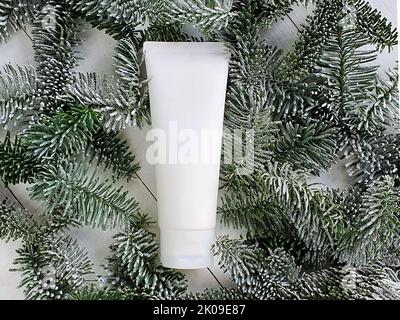 Unbranded white cosmetic products squeeze tube on white wooden background with snowy branches of christmas fir tree. Mockup, template. Container for b Stock Photo