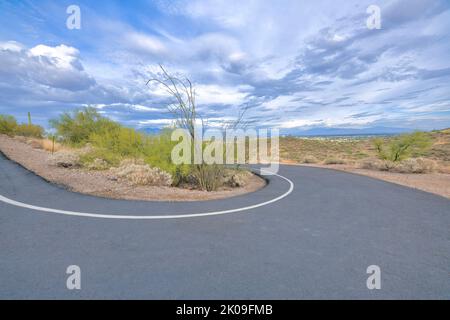 U-shaped concrete bicycle path and walking pathway in a nature park at Tucson, Arizona. Asphalt road with an overlooking view of slopes and mountains Stock Photo