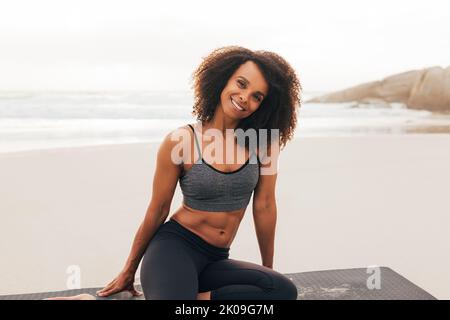 Portrait of a smiling beautiful woman looking at camera while sitting on mat at sunset Stock Photo