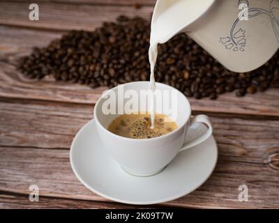 Pouring milk in a white cup of coffee. coffee beans in the background Stock Photo