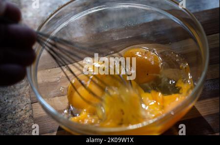 Whipping eggs in a glass bowl. Egg yolks and egg whites mixed with spices. Stock Photo