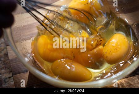 Whipping eggs in a glass bowl. Egg yolks and egg whites mixed with spices. Stock Photo