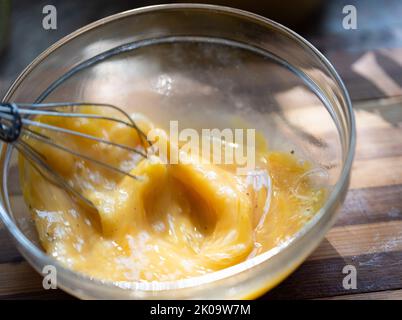 Whipping eggs in a glass bowl. Egg yolks and egg whites mixed with spices. Stock Photo
